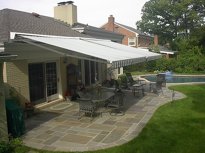 two retractable awnings side by side over a stone patio with a pool on the right